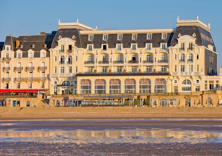 Exterior view of tan and gray hotel building with a beach in front