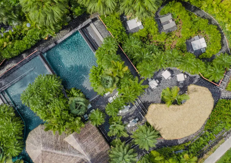 Top view of outdoor pool with straw hut coverings on the right of the pool