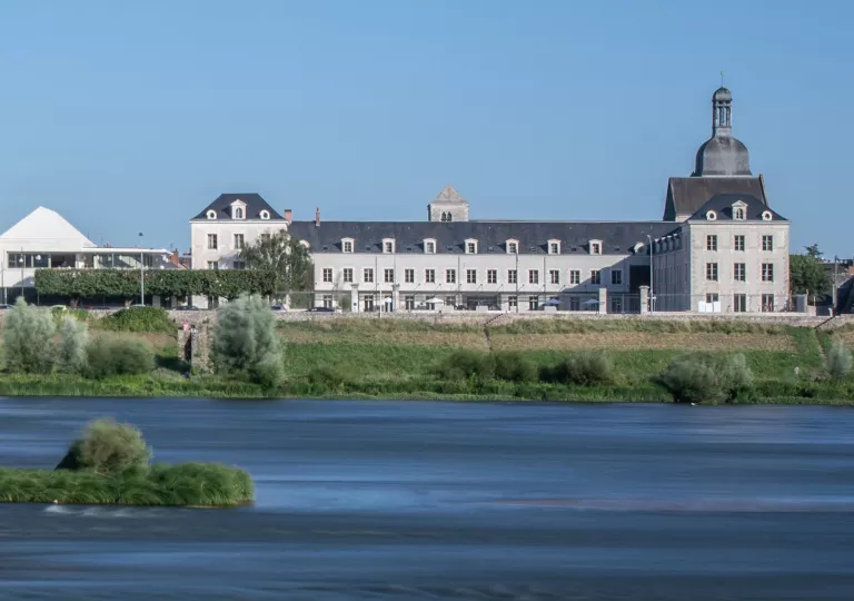 Wide, exterior view of a long hotel building behind a small lake