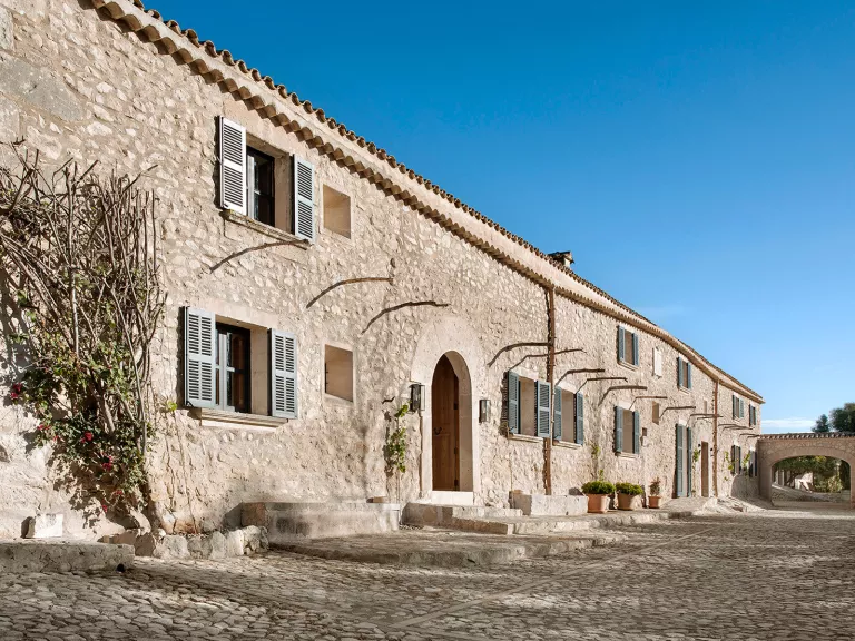 Long, stone building with a stone pathway and branches along the wall