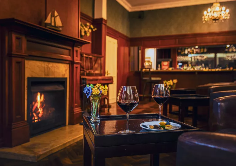 Table with two wine glasses in front of a fireplace in an indoor lounge