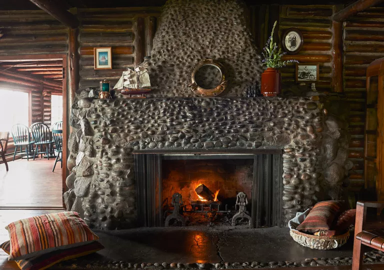 Fireplace made of stone, with a dining area to the left in a separate room