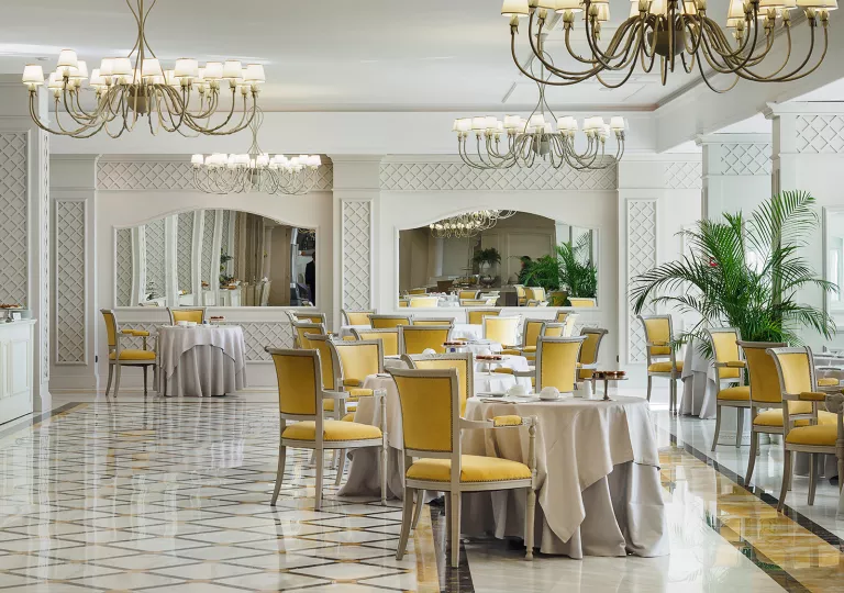 Indoor dining hall with white and yellow cushioned chairs and chandeliers on the ceilings