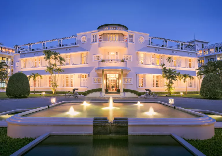 Exterior view of illuminated white building with an illuminated fountain in front