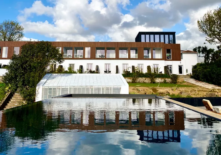 Exterior view of white and wooden building, with outdoor pool