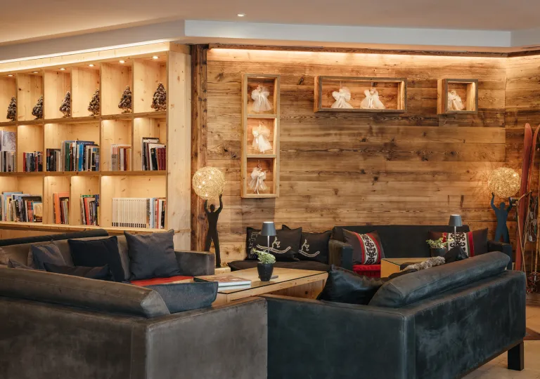 Library in a wooden cabin room, with books along the shelves and cushioned, gray couches