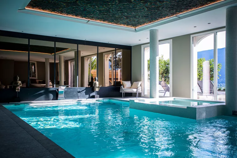 Indoor swimming pool with large mirrors and windows with views of an outdoor patio