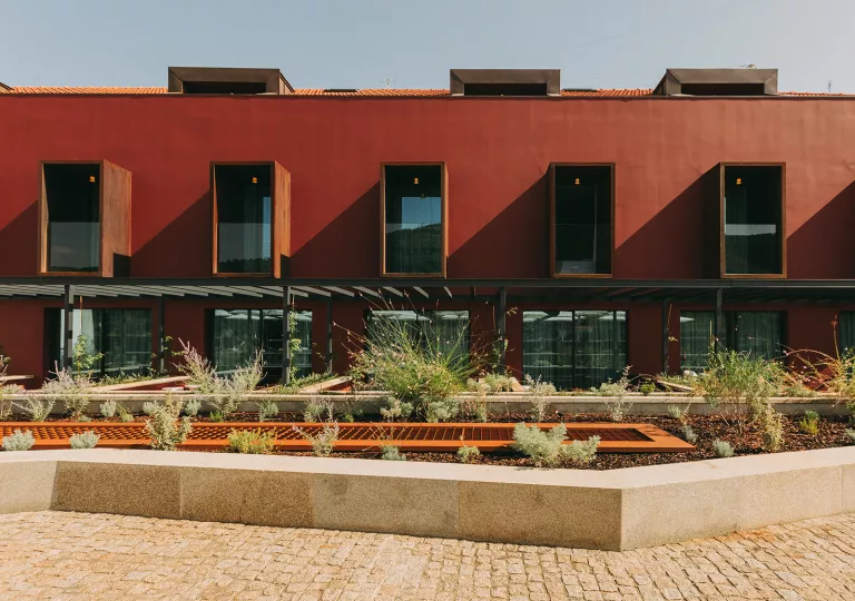 Exterior view of a red building with large windows and a small plant enclosure in front