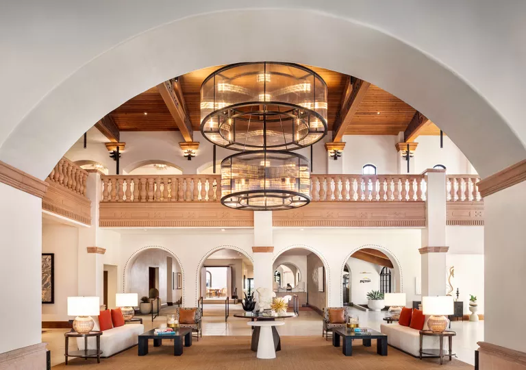 Indoor hotel lobby with large light fixture and cushioned sofas in front of smaller coffee tables