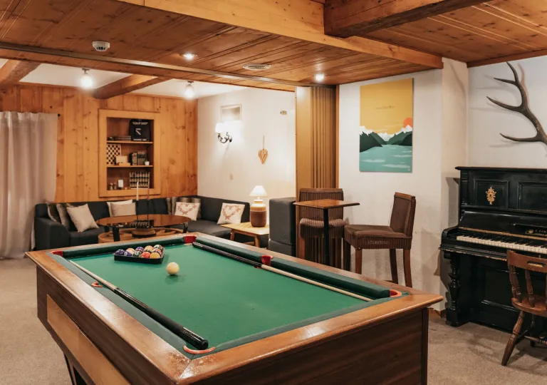 A rustic recreation room at Hôtel du Glacier, featuring a pool table, comfortable seating and a wooden piano against the wall.