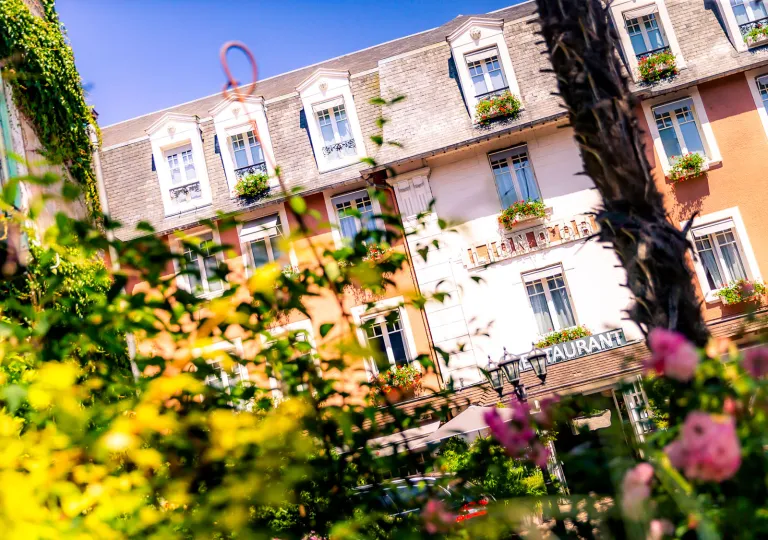 Exterior view of white and brown hotel building with plants and bushes in front