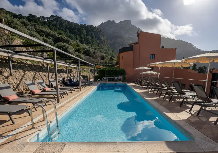 Outdoor pool surrounded by reclining chairs and an orange building in the background