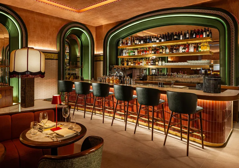 Bar and lounge with green arch doorways and green stools in front of a dimly lit bar counter