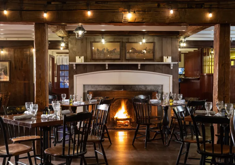Restaurant dining area with dark brown chairs and tables in front of a lit fireplace