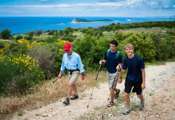 Three guests with hiking poles on coastal trail, ocean, small island chain in distance.