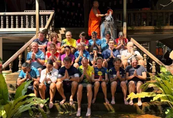 Group of people sitting on a flight of stairs, with a monk on top throwing water on them