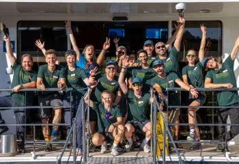 Group of people wearing green t-shirts, smiling with their arms in the air