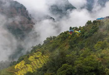 Hills with thick forest and houses on top, with fog in the background