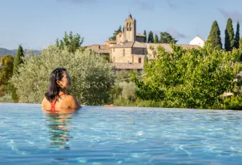 Woman leaning on the edge of an infinity pool, looking out towards a stone castle