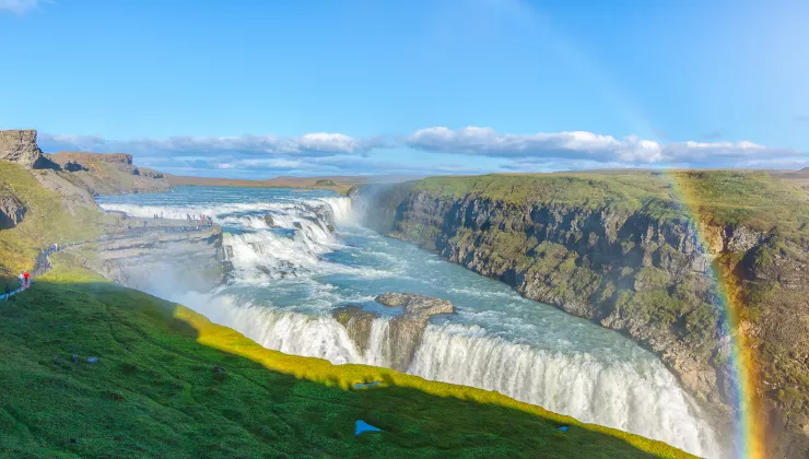 Wide shot of alpine vista, waterfall, rainbow, cliffs on either side. 