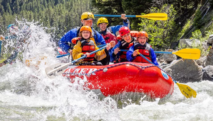 Group of adults and kids on a red raft in the middle of a river