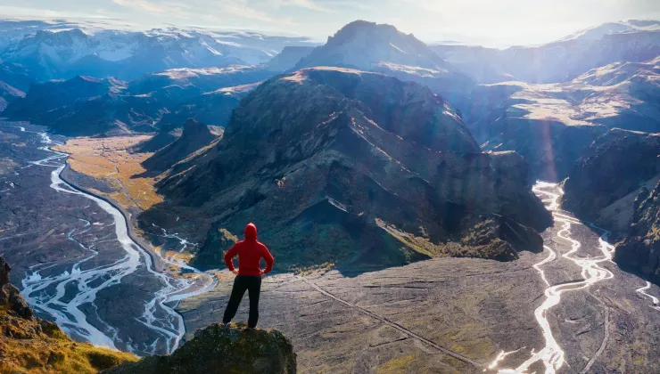Person standing on a cliff looking out towards tall mountains