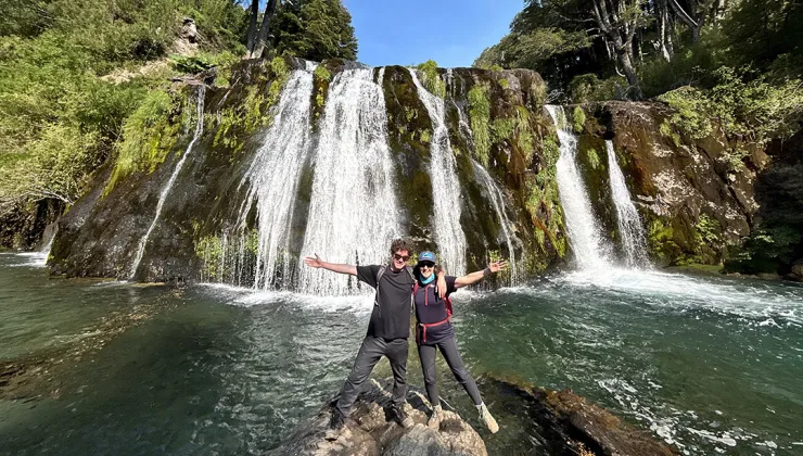 Man and woman with their arms open in front of a waterfall