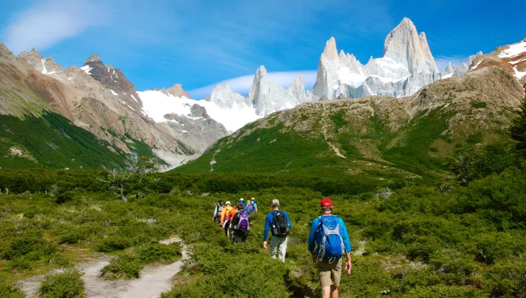 Group of people hiking on a grassy valley with snowy mountains in the distance