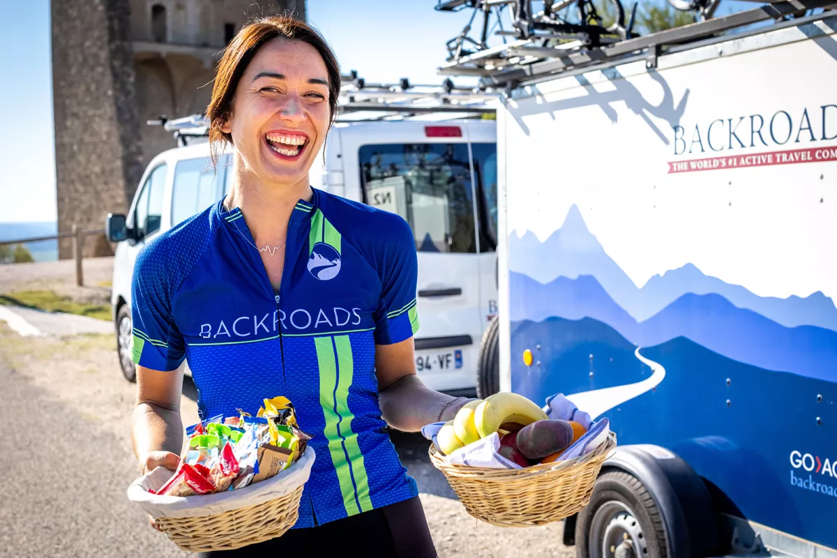 Woman holding two baskets full of fruits and snacks, in front of two Backroads labeled vans