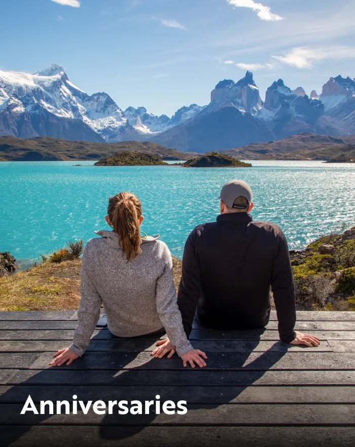 Man and woman sitting on a dock, looking out to a lake and large mountains