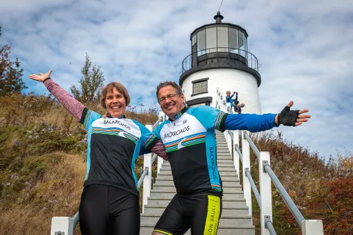 Two guests with their arms outstretched, lighthouse in background.