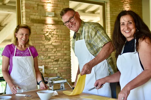 People smiling at the camera while rolling out pasta dough