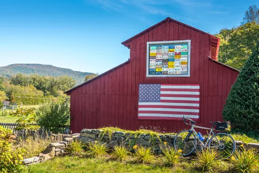 Shot of bike in front of red barn, US flag on barn wall.
