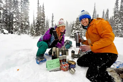 Two guests in snow, getting blueberry tea from thermos.