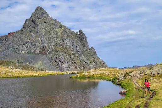 Guest next to small lake, large craggy mountain to her right.
