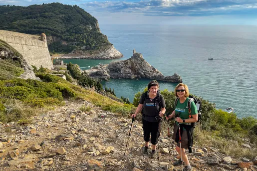 Two guests on rocky cliffside, Chiesa di San Pietro in distance.