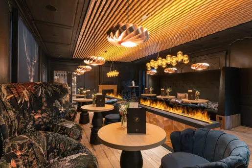 Bar and lounge with large cushioned chairs, circular tables and a fire pit in the center