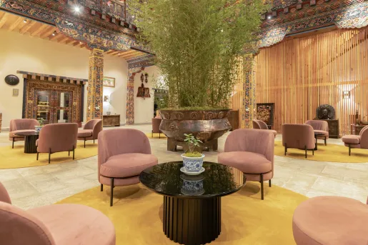 Indoor hotel lobby with pink, cushioned chairs and a large plant in he center