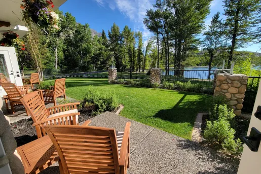 Wooden chairs in a stone patio, looking out to a grass field and a lake surrounded by trees