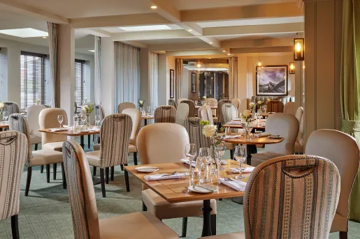 Indoor dining hall with tan chairs and wooden tables, with wine glasses on each table