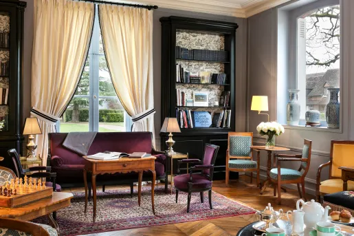 Library and lounge with tall, black book shelves and burgundy velvet sofas