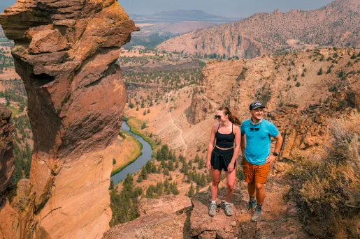 Man and woman on top of an orange cliff with large canyons in the background