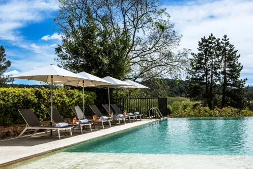 Outdoor pool surrounded by gray, reclining chairs and white umbrellas