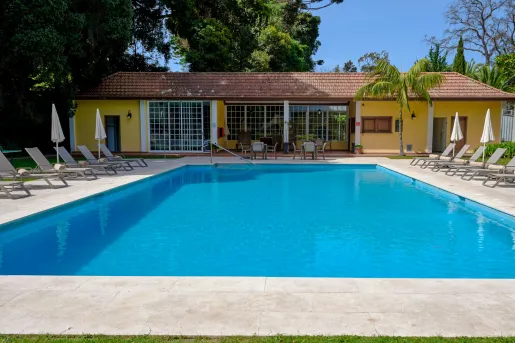 Outdoor pool with a yellow building and pool chairs and umbrellas