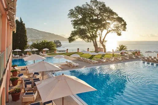Two outdoor pools with umbrellas and pool chairs along the perimeter