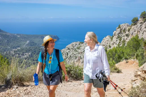 Two women smiling at each other while walking on a dirt trail