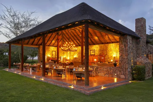 Outdoor, open dining patio with a chandelier, surrounded by a grassy area
