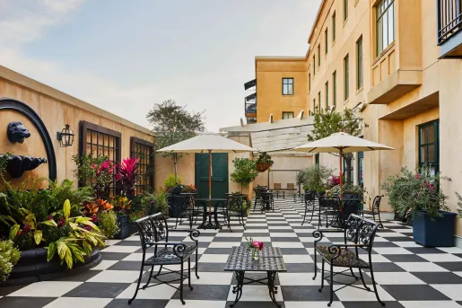 Outdoor patio with black and white checkered flooring, large plants and yellows buildings surrounding
