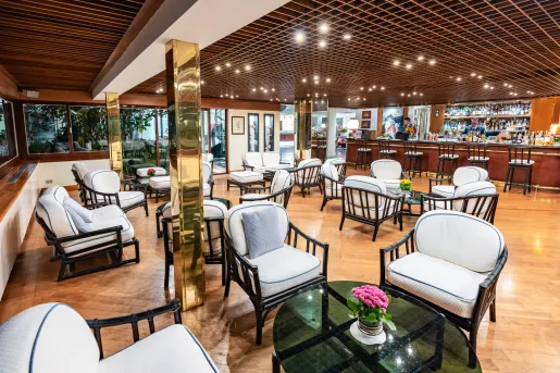 Bar and lounge with white, cushioned chairs and circular glass tables