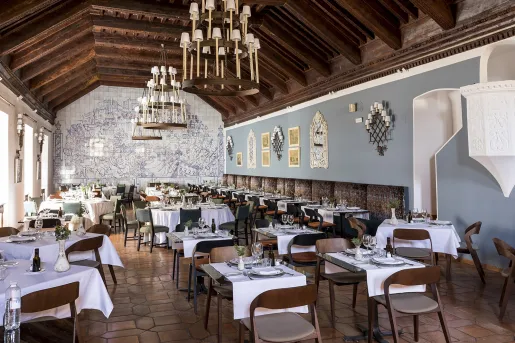 Large dining hall with tables and wooden chairs, with three large candle chandeliers